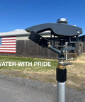 Close-up of Beefy Tripod Sprinkler With 125 Ft Coverage in a field, American flag on building in background, water with pride text.