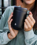Self Heating Coffee Mug With Rechargeable Battery And Digital Temperature Control Keeps Your Drinks Piping Hot All Day Long sleek black mug held by person wearing a soft green top