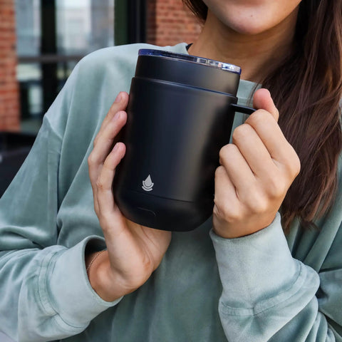 Self Heating Coffee Mug With Rechargeable Battery And Digital Temperature Control Keeps Your Drinks Piping Hot All Day Long sleek black mug held by person wearing a soft green top