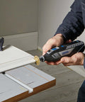 Dremel 8250-5 cordless rotary tool with sanding wheel attached, blue/black body, in use on wood.