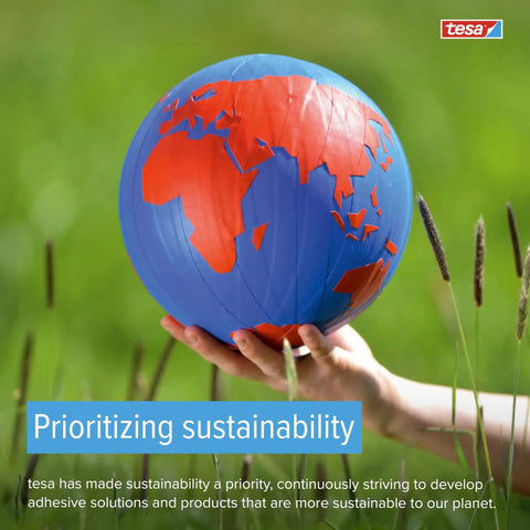 Hand holding blue and red globe in grassy field, promoting sustainability focus by tesa with prioritizing sustainability text.