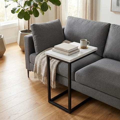 C Shaped Metal Side Table With Genuine White Marble Top For Living Room Or Home Office Space Saving End Table That Slides Under Sofa 18 In Wide By 24 In High Sleek And Slick Modern Accent next to gray sofa with books and mug on top.