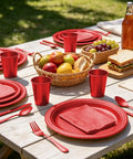 Kickback Ready Red Plastic Dinnerware Set Feeds Fifty Guests With Nine Inch Plates Seven Inch Snack Plates 12 Ounce Cups Utensils And Napkins For No Stress Backyard Hangouts laid out on a picnic table.