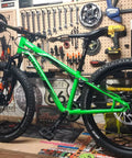 Green mountain bike on workbench in workshop with tools on wall.