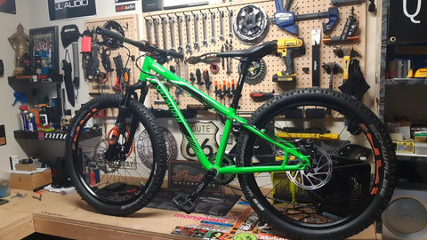 Green mountain bike on workbench in workshop with tools on wall.