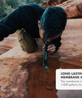 Individual using Personal Water Purifier For Hiking Camping Travel And Emergency Prep Delivers Safe Drinking Water By Filtering Out Bacteria Parasites And Microplastics So You Can Stay Ready For Any Backcountry Adventure to drink from rock pool.