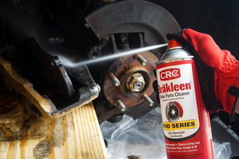 CRC Brakleen brake parts cleaner spray used on rusty brake rotor and hub, red-gloved hand