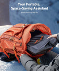 Orange backpack being packed with gear on a snowy background.