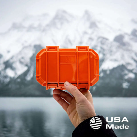 Micro Waterproof Dry Box Case Yellow IP67 Lockable Hard Shell Container With Carabiner Loop For Earbuds PLB Iems And Small Medical Devices Usa Made in hand by lake with mountains