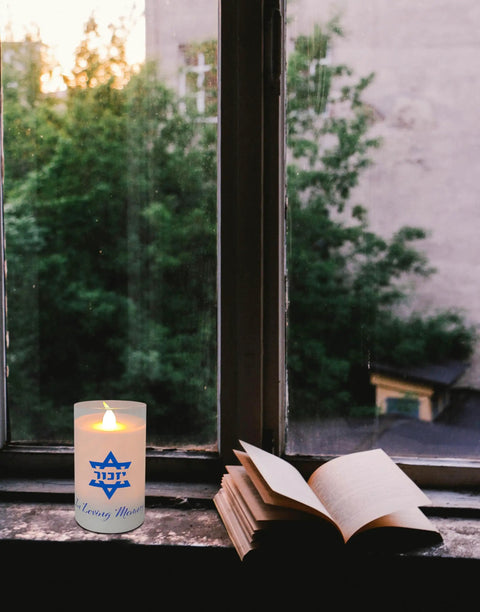 Electric Yahrzeit Candle LED Votive Flameless Memorial Light Battery Operated in a window with an open book nearby.