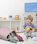 Child in playroom next to a Large Tall Cotton Rope Laundry Basket Hamper With Handles For Nursery And Living Room, Boho Style, Light Pink.