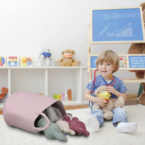 Child in playroom next to a Large Tall Cotton Rope Laundry Basket Hamper With Handles For Nursery And Living Room, Boho Style, Light Pink.