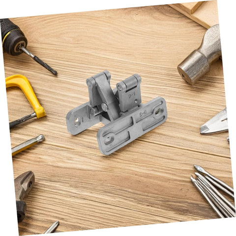 Angled front view of concealed stainless steel door hinge set on wooden workbench with drill and hammer nearby.