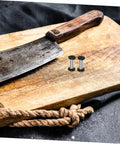 Badass Flat Head Knife Handle Screws And Brass Snap Rivets For Wood And Metal Crafts Tight Fit 2 Piece Kit on a cutting board with a knife.