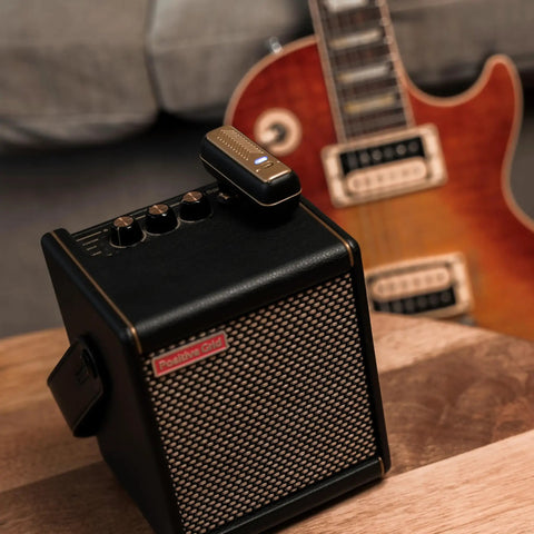 Wireless Guitar System With Rock-Solid 2.4G Transmission, 24-Bit/48kHz Audio beside guitar and amplifier on wooden table.