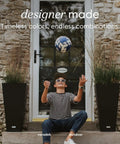 Outdoor setting with a boy playing soccer between two 30-inch black plastic resin taper planters on either side of a stone entrance.