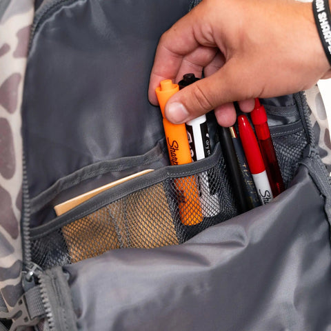 Hand organizing pens and highlighter in mesh pocket of Deer Camo Backpack For School And Everyday Outdoor Adventures 25L Capacity