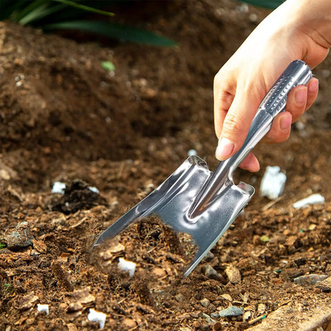 Hand using stainless steel garden trowel for transplanting in soil, part of the Stainless Steel Garden Shovel And Trowel Hand Tools Set For Transplanting Weeding Moving And Smoothing Digging And Planting Durable Ergonomic Do It All Three Pack For Small Gardens.