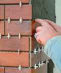 Hands placing 1200 Pcs Cross Shape Tile Spacers 1mm Gap For Ceramic Tile Installation, ensuring precise grout lines between red tiles on a wall.