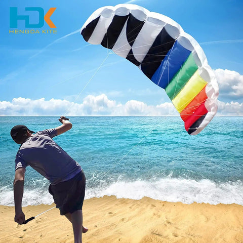 Person flying Rainbow Parafoil Kite 55 Inch Pro Stunt Soft Foil Design With 1.4 M Wing Span on beach with ocean background