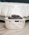 40 Liter Laundry Basket With Lightweight Plastic Build Ivory Wicker-Look Hamper beside a bed in a bedroom.