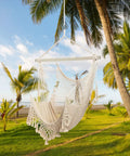 Cozy Cotton Rope Hammock Chair With 330Lb Weight Capacity hanging outdoors, soft beige rope and sturdy metal rod amid palm trees.