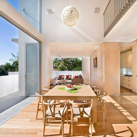 Modern dining area with wooden table and chairs, large windows, and natural light flooding the space, interior view.