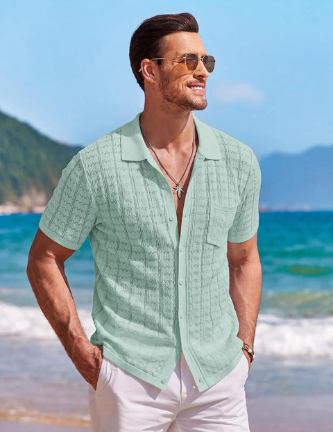 Man wearing Men's Knit Short Sleeve Button Down Shirt Vintage Polo Beach Top in Ice Green, standing on beach with mountains.