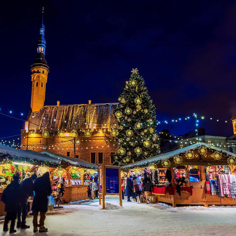 Christmas market scene with lit stalls and large decorated Christmas tree in front of historic building at night