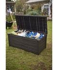 Lockable 120 Gallon Outdoor Storage Deck Box in brown with lid open, showing cushions, tools, and pool toys in garden setting