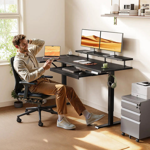 Man working at 55 Inch L Shaped Electric Standing Desk With Keyboard Tray And Reversible Height Adjustment, Corner Computer Desk With Monitor Stand, Sit Stand Lift Table For Home Office, Carbon Fiber Black