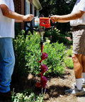 Two people using Partner Up 1 Or 2 Man Earth Auger With 52cc 2 Cycle Engine and Extension, dual throttle handles, in garden