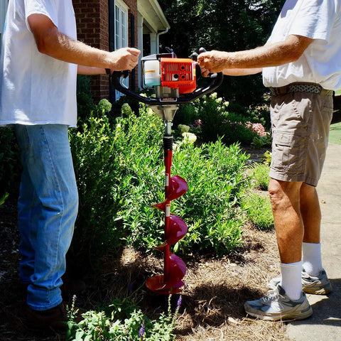 Two people using Partner Up 1 Or 2 Man Earth Auger With 52cc 2 Cycle Engine and Extension, dual throttle handles, in garden