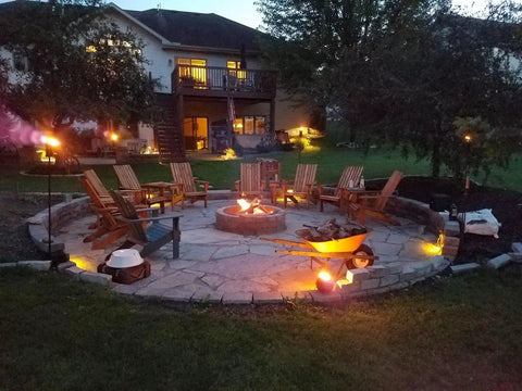 Night view of patio with chairs around a fire pit, lit by Three LED Landscape Lights With Bracket In Textured Architectural Bronze Finish 4 Pack.