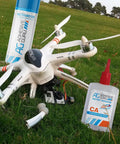 Two Adhesive Guru CA Glue bottles with Activator beside a white quadcopter drone on grass