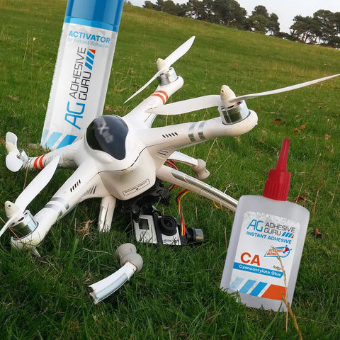 Two Adhesive Guru CA Glue bottles with Activator beside a white quadcopter drone on grass