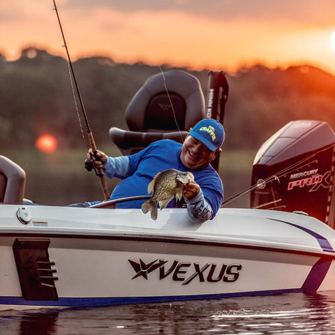 Fisherman holding a fish on a boat at sunset, using Wally Marshall Signature Series Underspin Fishing Reel With All Metal Gears 2 Plus 1 Bearings 4 Point 3 To 1 Gear Ratio Reversible Handle Smooth Casting And Retrieval For Easy No Fuss Fishing.