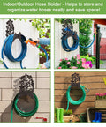 Cast Iron Garden Hose Holder Wall Mount For Outdoor Use Hose Hanger And Reel Storage Organizer Rack Keeps Hoses Neat And Off The Ground Heavy Duty Decorative Water Hose Storage For Garden Lawn Patio mounted on wall with green hose.