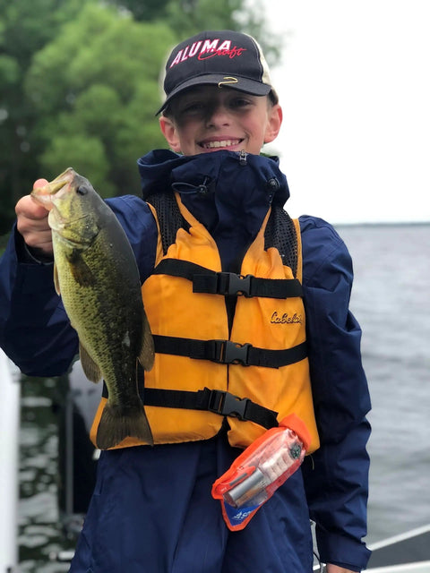 Smiling child holding fish on boat, wearing life jacket with Waterproof Survival Kit In A Rugged Bag With Emergency Thermal Blanket visible.