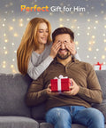 Woman surprising a man with a gift on a sofa, festive lights in the background, perfect romantic gesture.