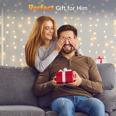Woman surprising a man with a gift on a sofa, festive lights in the background, perfect romantic gesture.