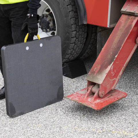 Person holding HDPE Outrigger Pad 24x24x1 Inch Beefy Heavy Duty Jack Pad next to tire and metal jack arm with rope handle visible