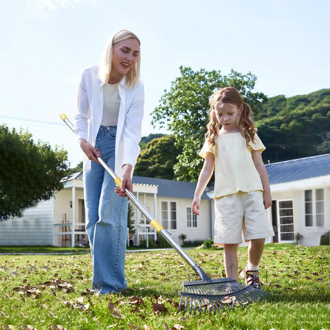 Two people using Heavy Duty Wide Garden Leaf Rake With Adjustable Long Handle For Yard And Lawn Cleanup on grassy lawn.