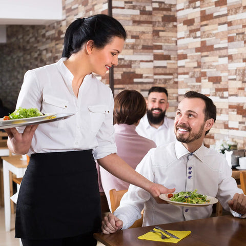 Waitstaff in black pro waist apron with 3 pockets serving salad, restaurant setting, wearing water-resistant durable polyester half apron.