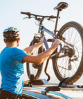 Person in helmet securing bicycle on a car roof rack using Four Pack Tie Down Straps 0.78 Inch Wide By 5 Foot Long With Buckles.