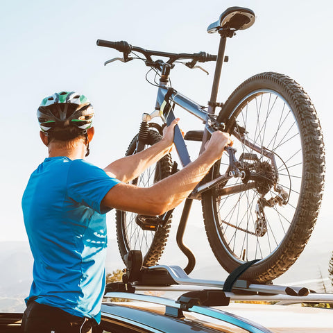 Person in helmet securing bicycle on a car roof rack using Four Pack Tie Down Straps 0.78 Inch Wide By 5 Foot Long With Buckles.