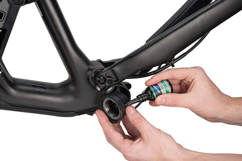 Close-up Park Tool RC-1 press-fit retaining compound bottle being applied to bicycle bottom bracket on matte black frame.
