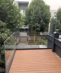 Heavy Duty Glass Railing System For Deck And Balcony Featuring Rock Solid Spigot Clamps With Flexible Floor Or Side Mount Hardware And Premium Aluminum Posts In Matte Black Covers For Quick Pool And Yard Fence Projects on a wooden deck.