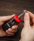 Hand holding Stubby Ratcheting Screwdriver Kit With 14-In-1 Mini Bit Set Including Flathead, Hex, Torx, Square, And Pozidriv Tips Compact Black And Red Dope Handy Tool For Quick Fixes And Electronics Projects on wooden background