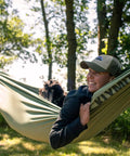 Person relaxing in a green camping hammock with dog in woods, enjoying outdoor adventures